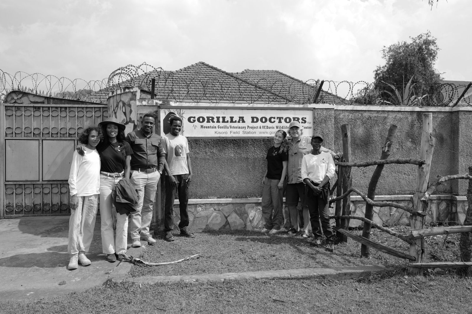The Saint Barth team standing with Gorilla Doctors staff in front of the Gorilla Doctors Kisoro Field Station sign, in black and white