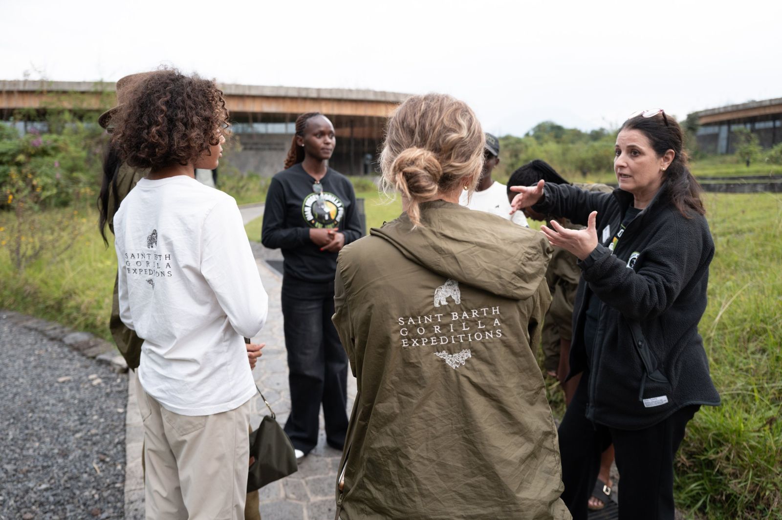 Guests wearing Saint Barth Gorilla Expeditions jackets listen to a conservation team member speaking outdoors