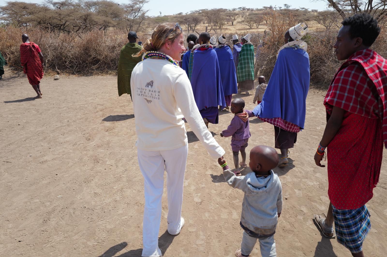 A visitor holds the hand of a small child while walking with Maasai community members in Tanzania